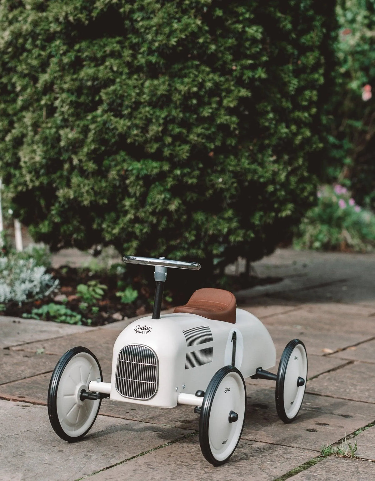 Vilac metal ride-on car in Cream on a patio