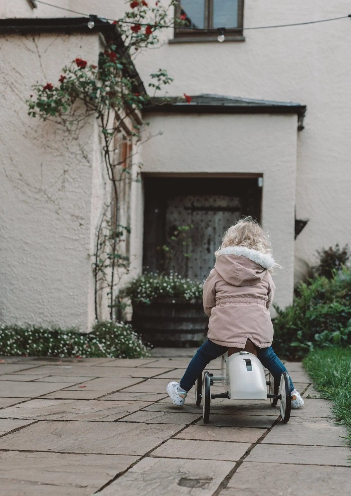 Toddler riding the Vilac car towards the house
